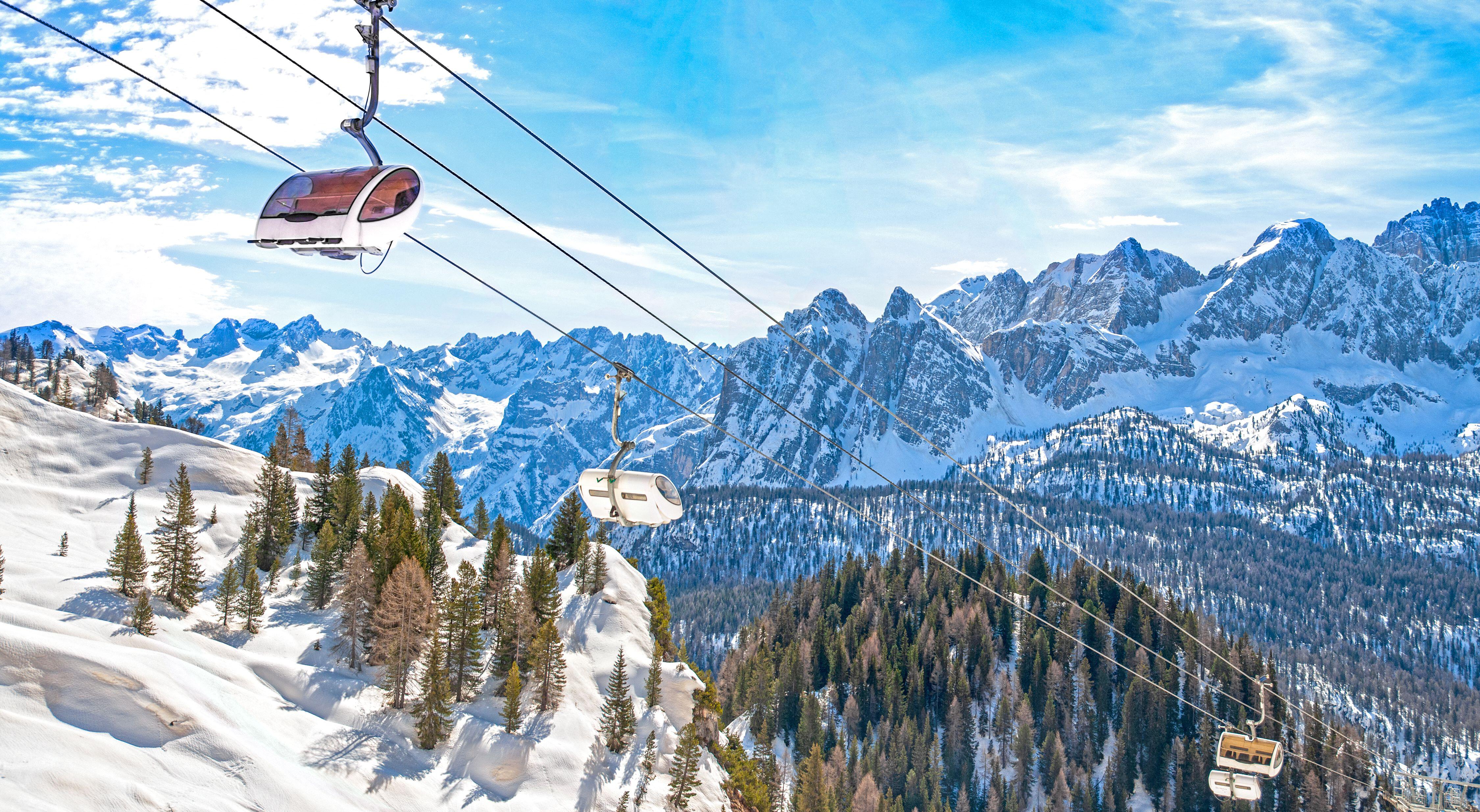 Ski lift with gondolas and chairs above a snowy mountain landscape in the Dolomites.