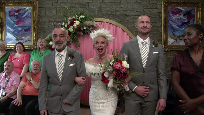 02_01_coro_debbie_choir_03 Kevin and Carl, wearing grey suits, walk sister Debbie, who is wearing a white wedding dress and elaborate headdress, down the aisle in Coronation Street