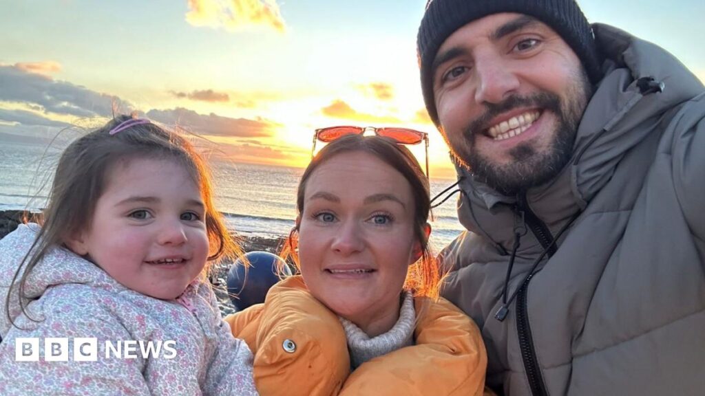 Owain’s Law: Wife takes campaign for brain tumour tissue changes to Parliament A woman and her husband pose with their young daughter, all wearing coats, at the seaside.