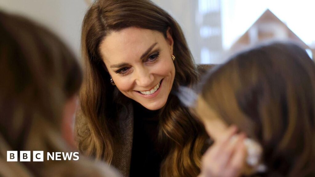 Princess of Wales visits ‘gold dust’ Yorkshire community groups The princess outdoors, speaking with a small group of people who are gathered around her. She is dressed warmly in an olive‑green coat, a matching flat cap, and a thick scarf wrapped around her neck. Her hands are clasped together at chest height.