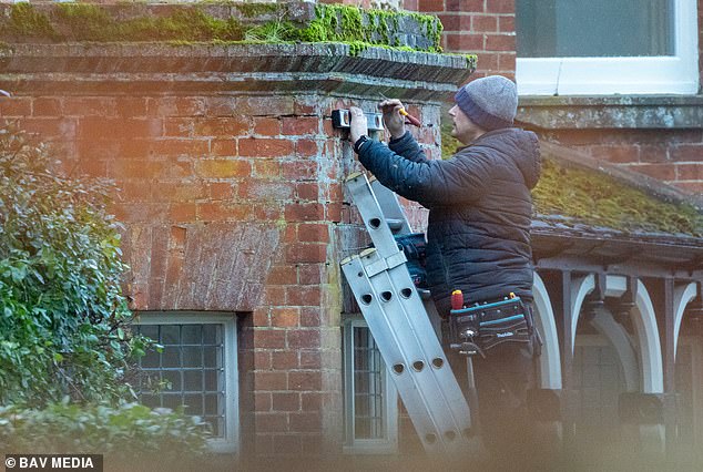 A workman measures up for the installation of new security lights on one of the red brick walls