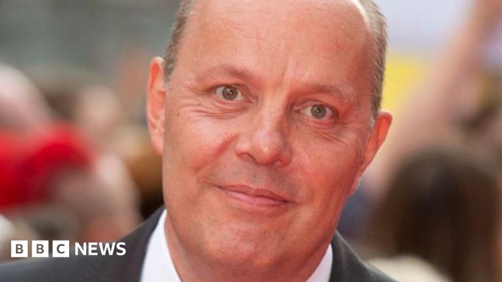 A close up of a man in a black suit and white shirt.