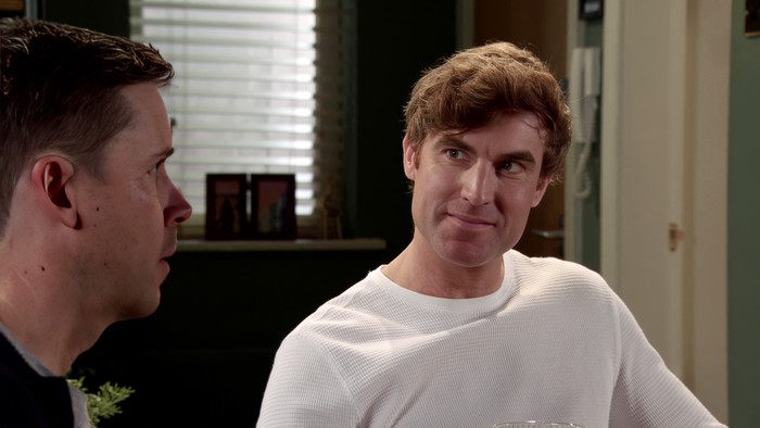 17_12_coro_todd_george_theo_03 Theo, wearing a white t-shirt, looks towards Todd in a scene from Coronation Street