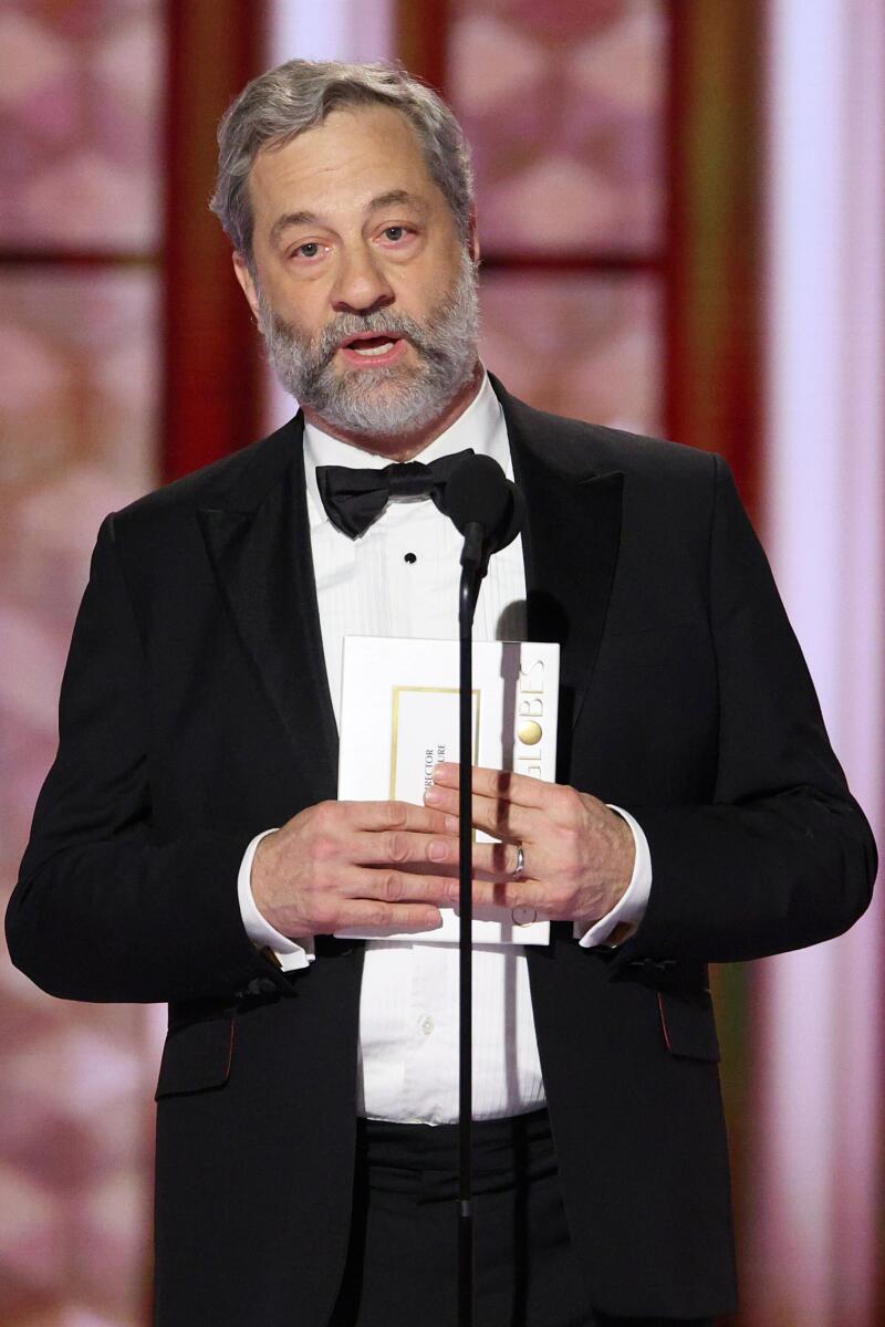 A man in a tuxedo at a microphone stand holding a card.