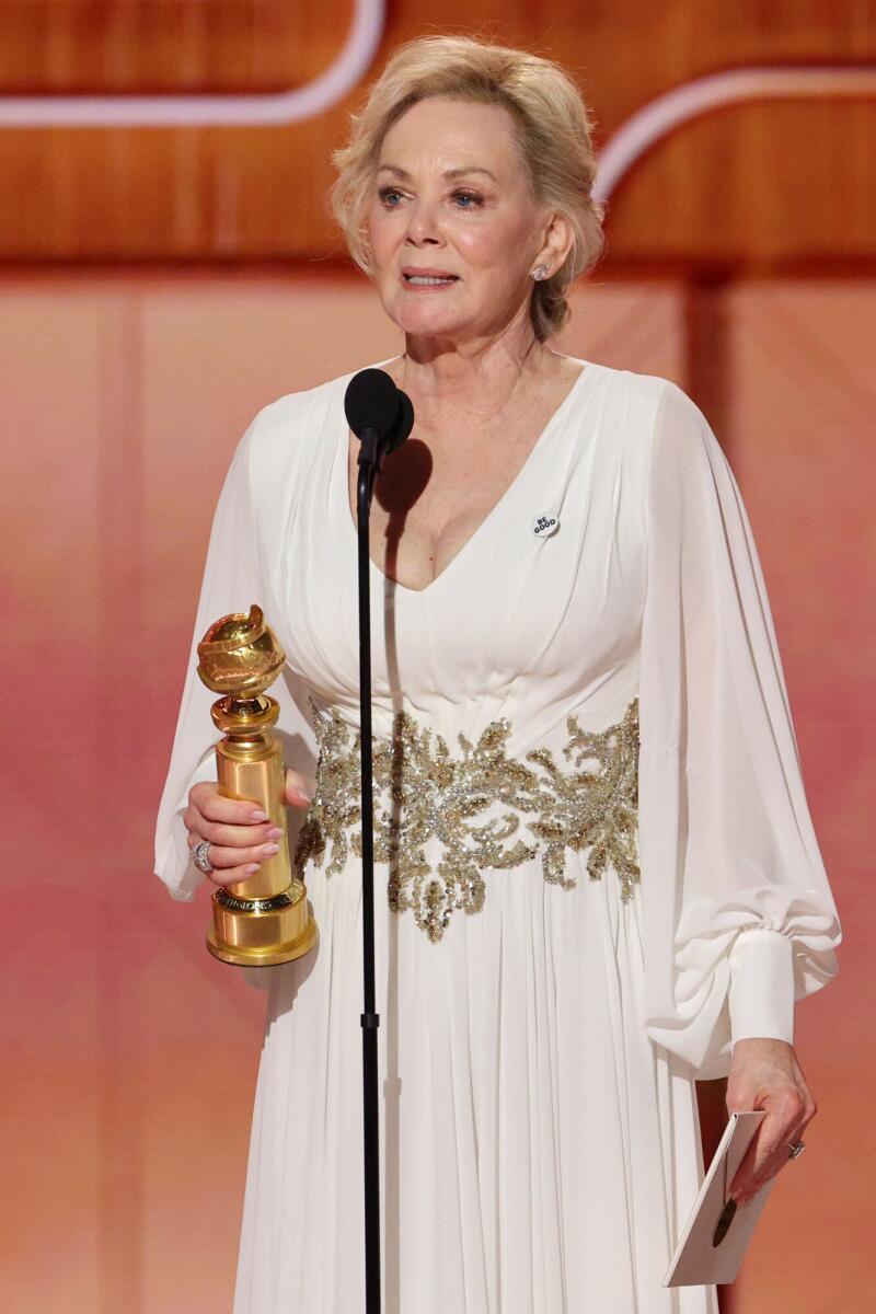 A woman in a white gown with a golden belt holding a gold trophy in her hand. 