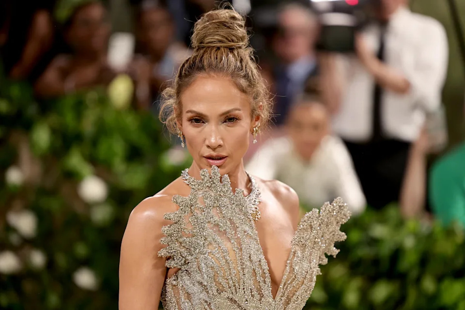 I don’t know who this is, but they are on a red carpet wearing an intricate, shimmering outfit with a feather-like pattern and an elegant updo hairstyle