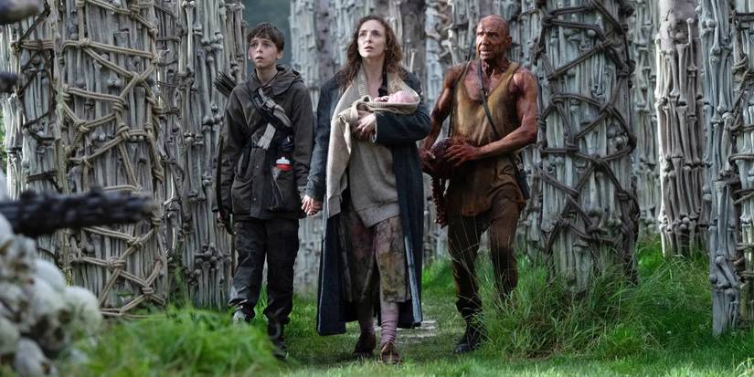 Alfie Williams as Spike, Jodie Comer as Isla, and Ralph Fiennes as Dr. Ian Kelson looking up at bone temple in 28 Years Later