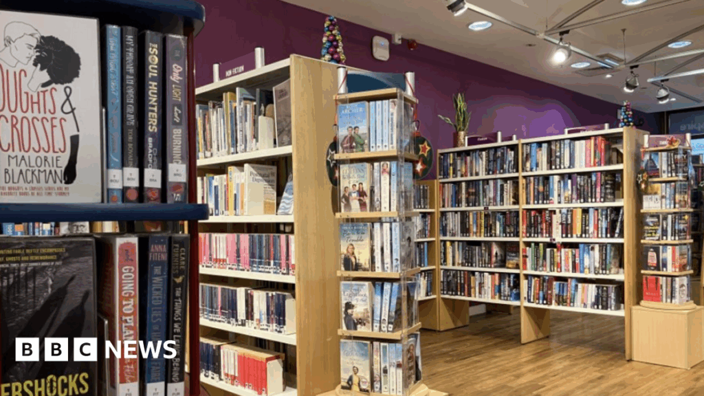 Several wooden shelving units are filled with books. The walls are painted purple and the flooring is wood.