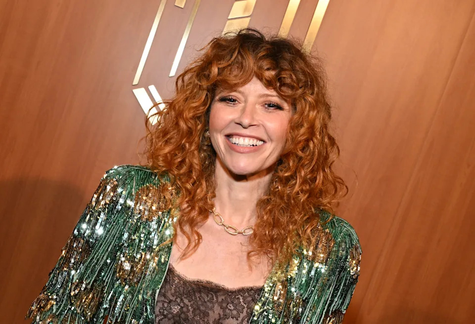 Natasha Lyonne smiling at an event, wearing a sequined, tasseled jacket over a lace top