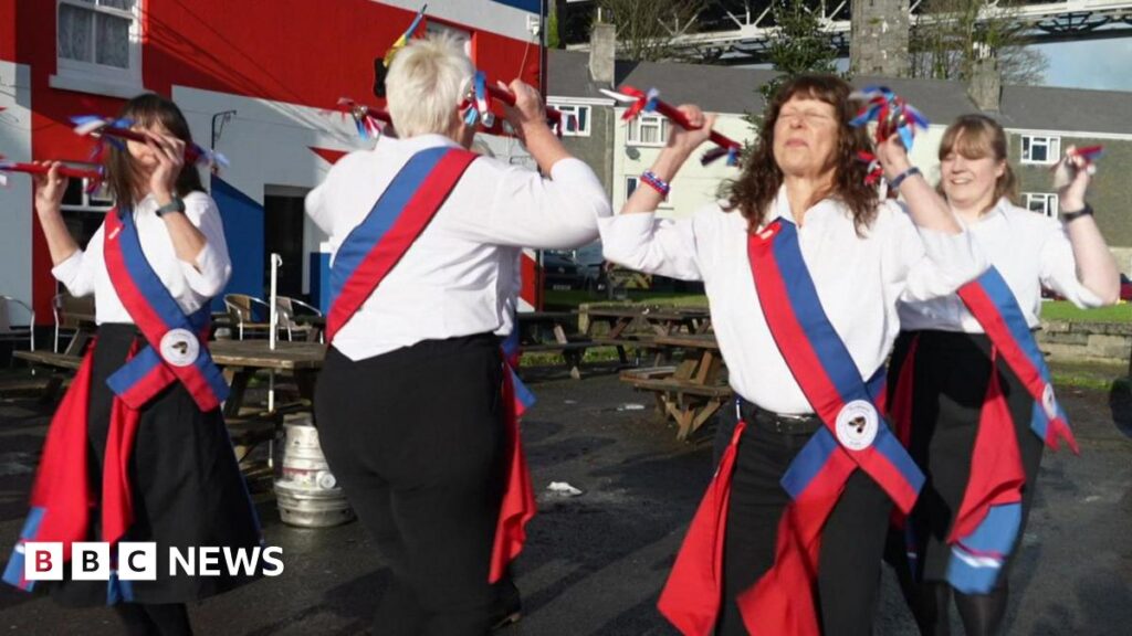 Devon clog dancers appeal in bid to keep tradition alive Five people clog dancing outside in the sunshine. They are all wearing white shirts with black trousers and red and blue sash's.