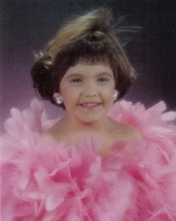 A little girl wears big earrings and a fluffy pink feathered boa
