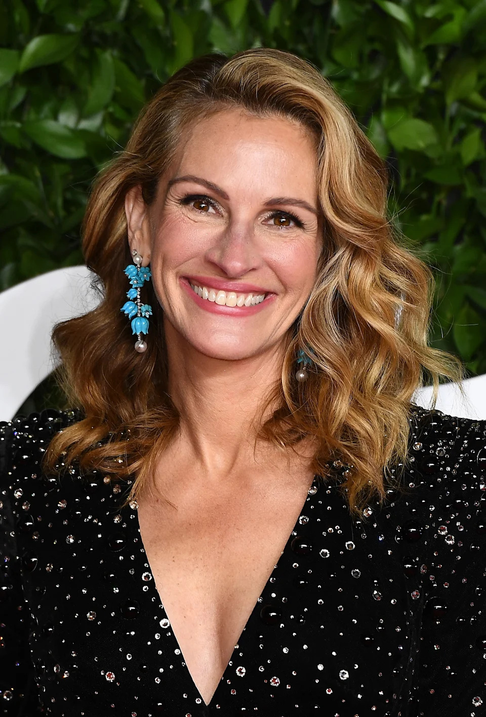 Person in a sequined dress with curly hair, smiling at a formal event, wearing statement earrings