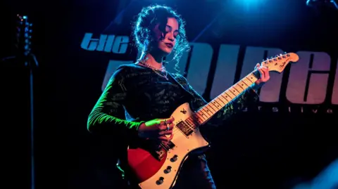 MVT A young woman plays an electric guitar on The Joiners stage.