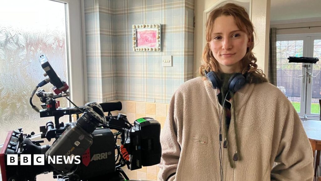 Sienna Rose, a woman with dark curly hair seen in a sepia-toned image with eyes closed, wearing large hoop earrings and singing into an old-fashioned microphone