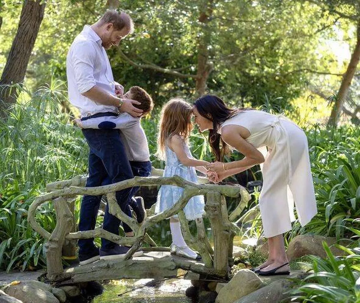 Prince Harry, Prince Archie, Princess Lilibet and Meghan Markle standing on a small bridge in sunshine