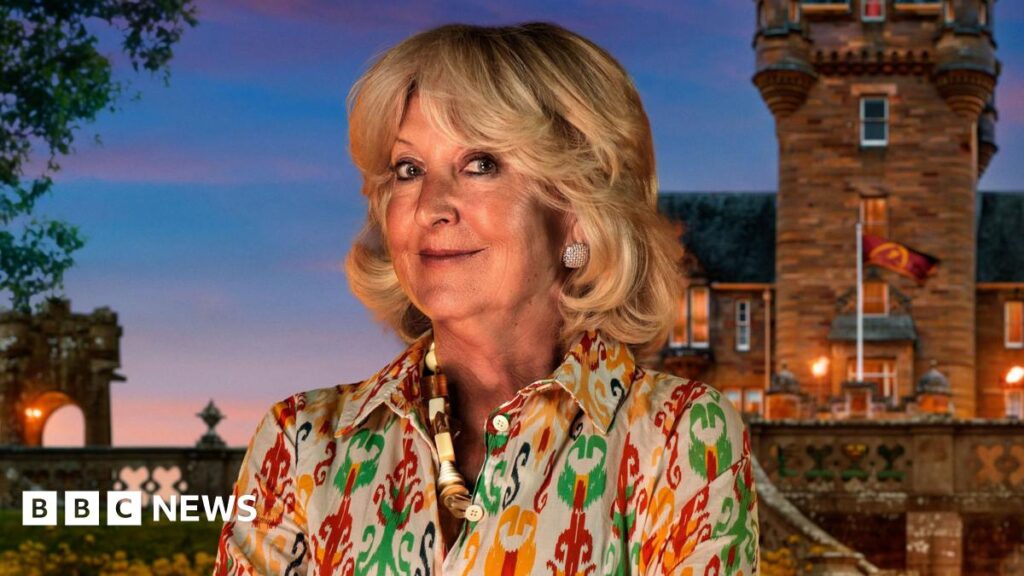 The Traitors: Does a Welsh accent help or is it a hindrance on the show? – BBC Handout photo of Fiona, one of the contestants in series four of BBC1's The Traitors. Fiona has short blown curled hair, blue eyes and smiles at the camera. She wears a yellow, green and red patterned blouse, a thick shell necklace and diamond earrings. A UGC image of the castle is seen in the background.