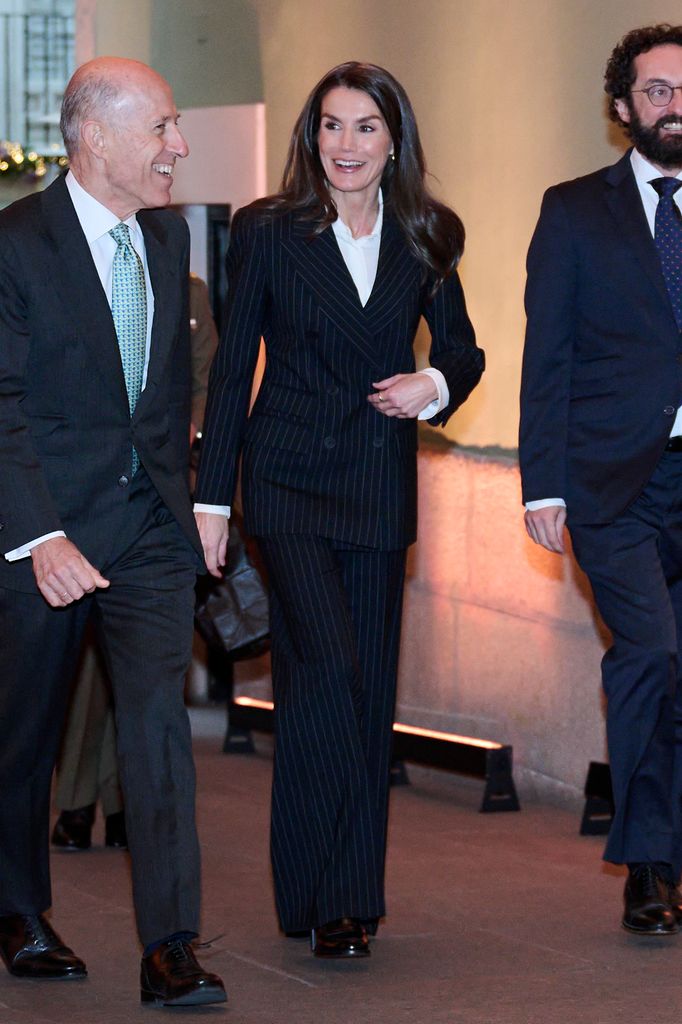 Queen Letizia walking in pinstripe suit between two men
