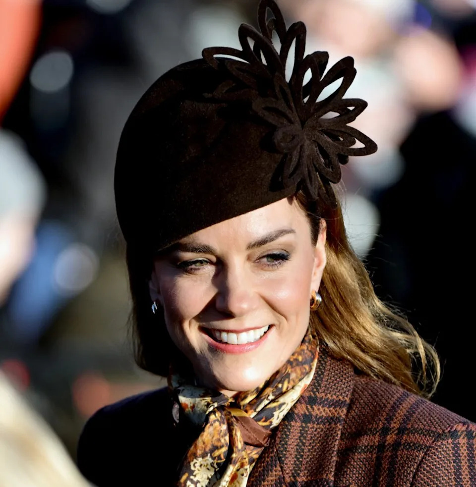  Princess Kate smiling, wearing a brown plaid coat and brown hat. 