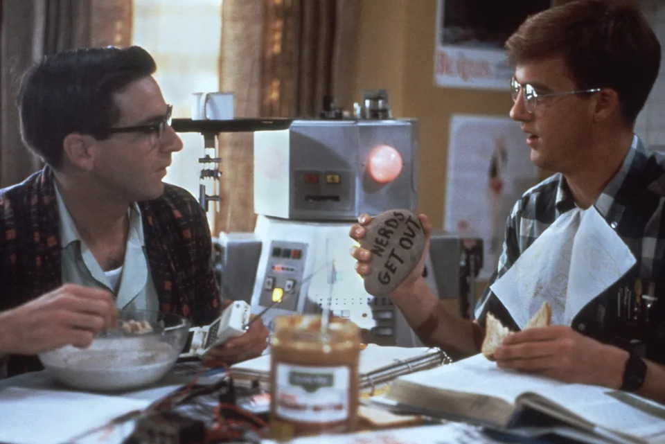 Robert Carradine and Anthony Edwards with a rock that reads, "nerds get out"