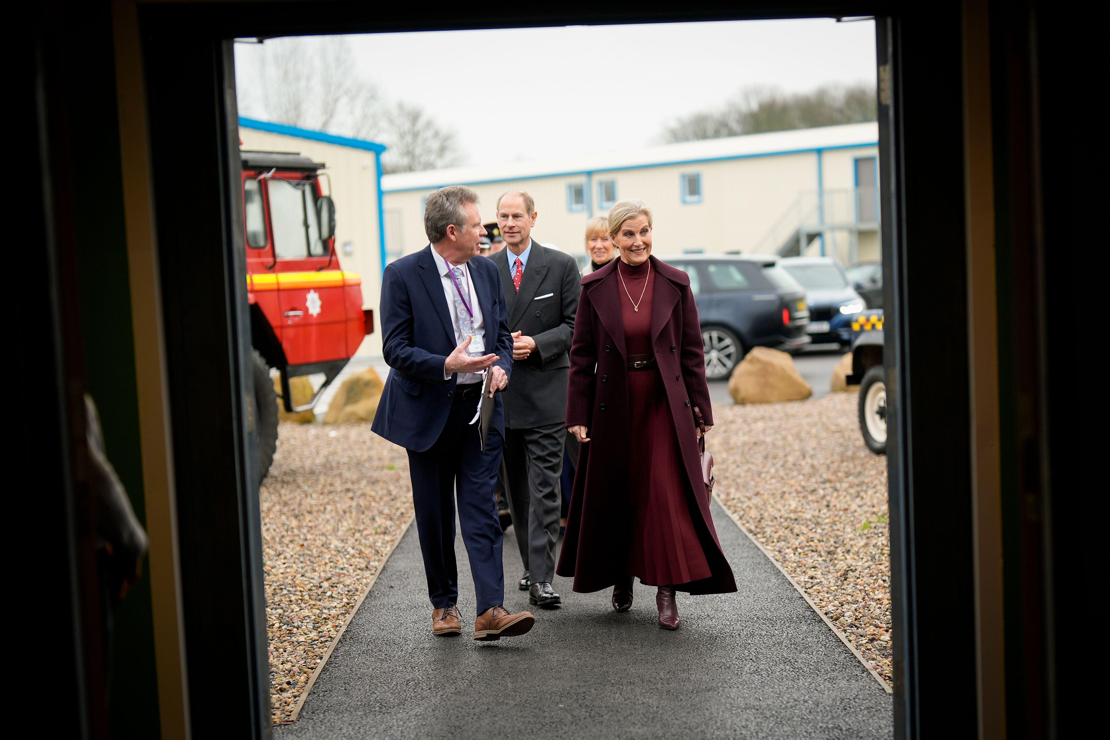 Duchess Sophie walking into a building with Prince Edward wearing a long maroon coat