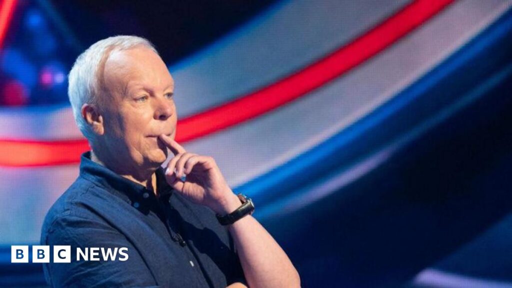 Actor Steve Pemberton wearing a navy short-sleeved shirt appearing on BBC One's The Weakest Link. He has his finger over his mouth as he answers a question.