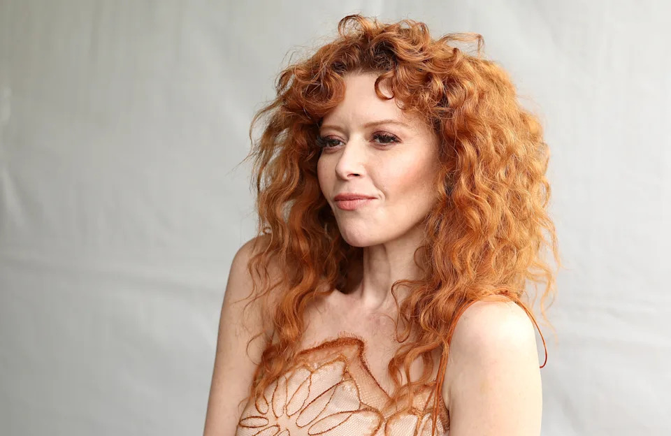 Natasha Lyonne with wavy hair in a sleeveless, textured dress, looking to the side at an event
