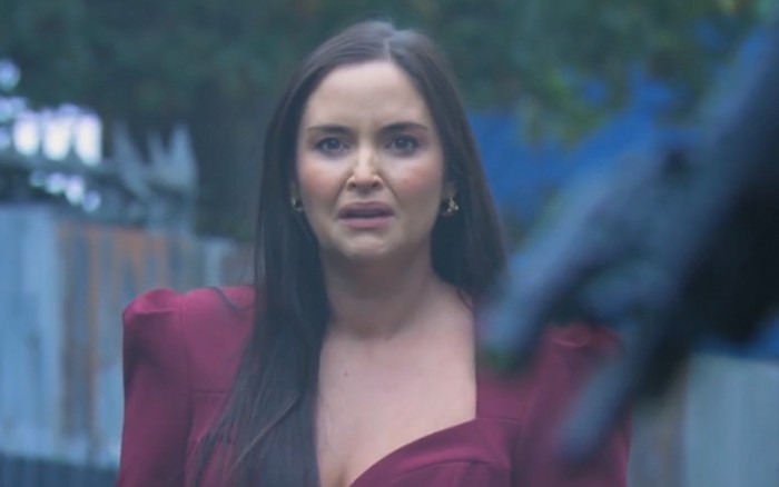 Jacqueline Jossa as Lauren Beale looking shocked in a burgundy dress while on the street with a gun out of focus in front of her for EastEnders.