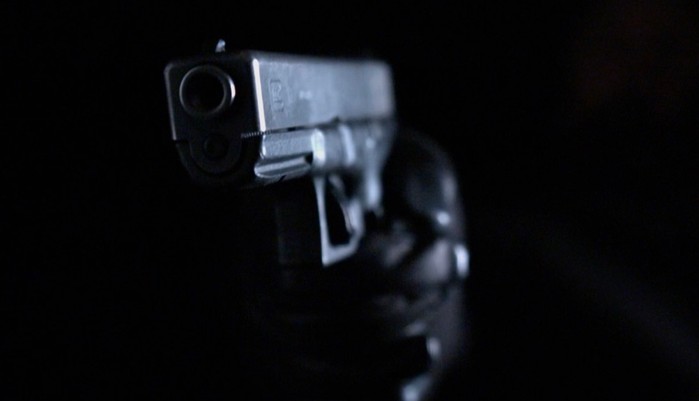 A hand in a black leather glove holds a gun from the shadows in EastEnders.