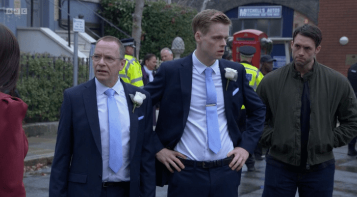 Adam Woodyatt as Ian Beale, Pierre Counihan-Moullier as Oscar Branning, and Stephen Aaron-Sipple as 'Man' on the street with police in the background in EastEnders.