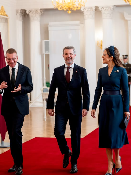 King Frederik, in a dark suit, and Queen Mary, in a navy dress with pearl brooch, talk to the President of Latvia