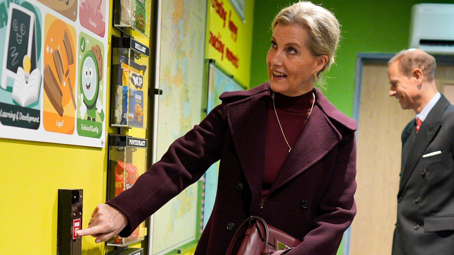 Duchess Sophie wearing a maroon dress and coat pressing a button on a wall