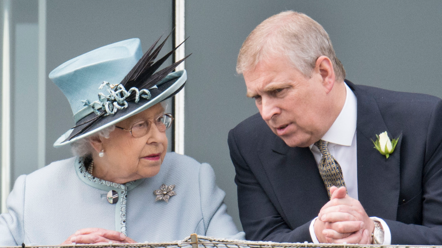 Queen Elizabeth in a blue coat and hat leaning forward and talking to Andrew Mountbatten-Windsor at the Epsom Derby