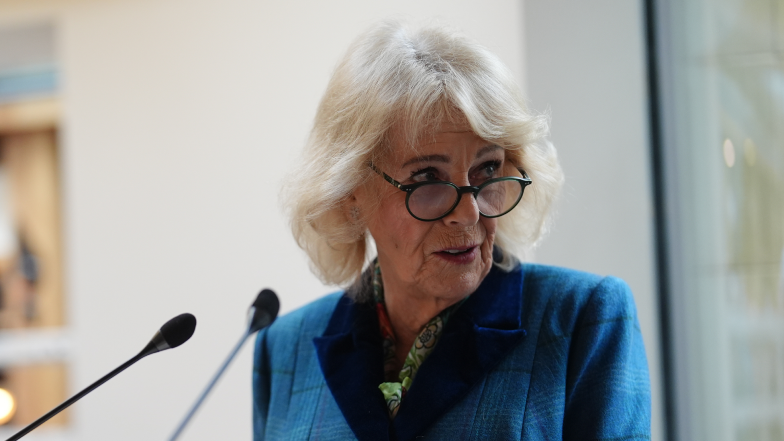 Queen Camilla speaking into a mic and wearing a blue suit