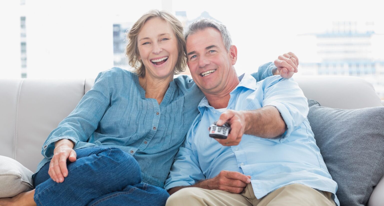 Flashback to 1996: Five Movies Turning 30 You Can Stream Right Now Cheerful couple cuddling and sitting on the couch watching tv at home in the living room