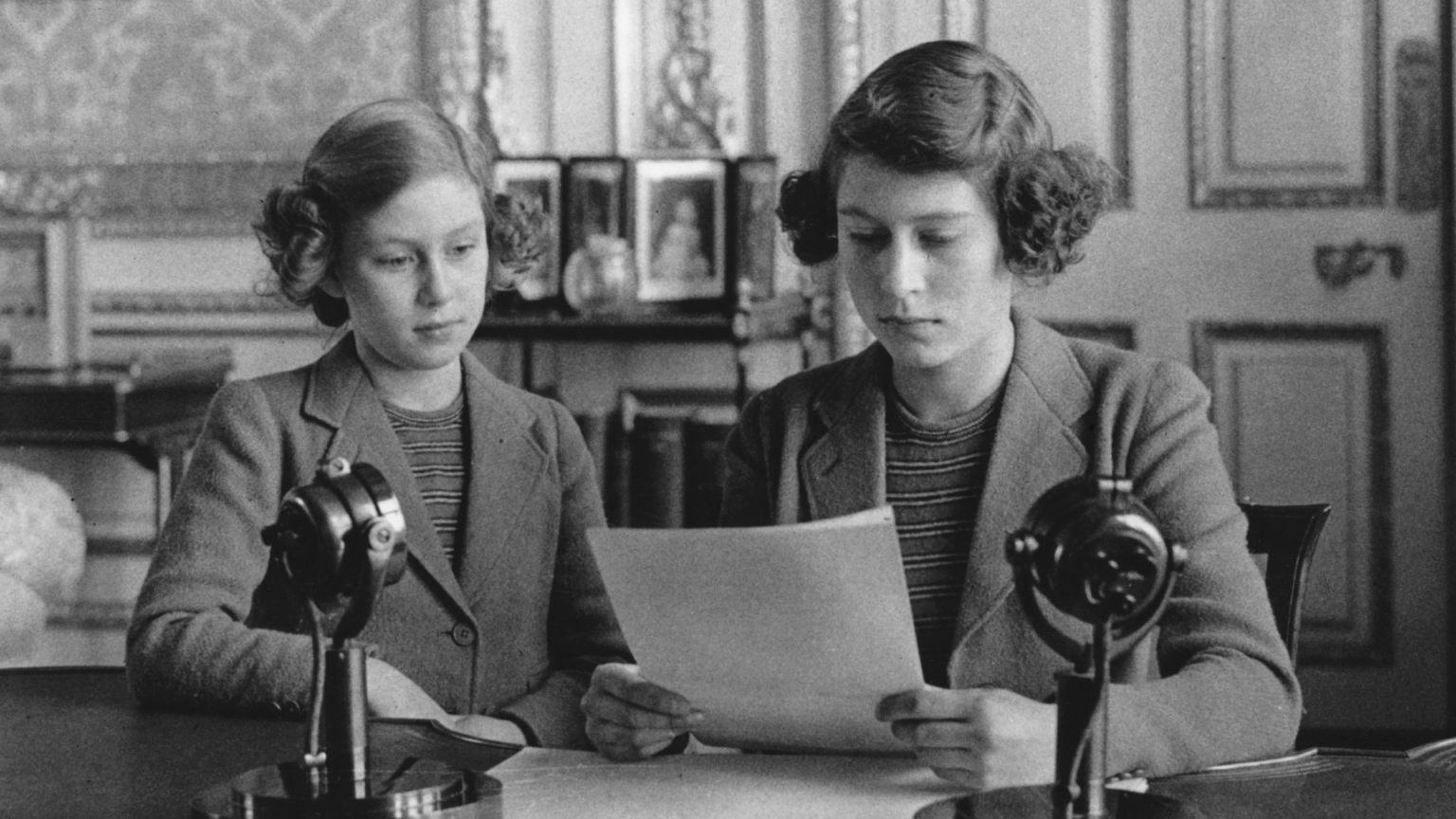 Princess Elizabeth and Princess Margaret reading off a paper at a desk