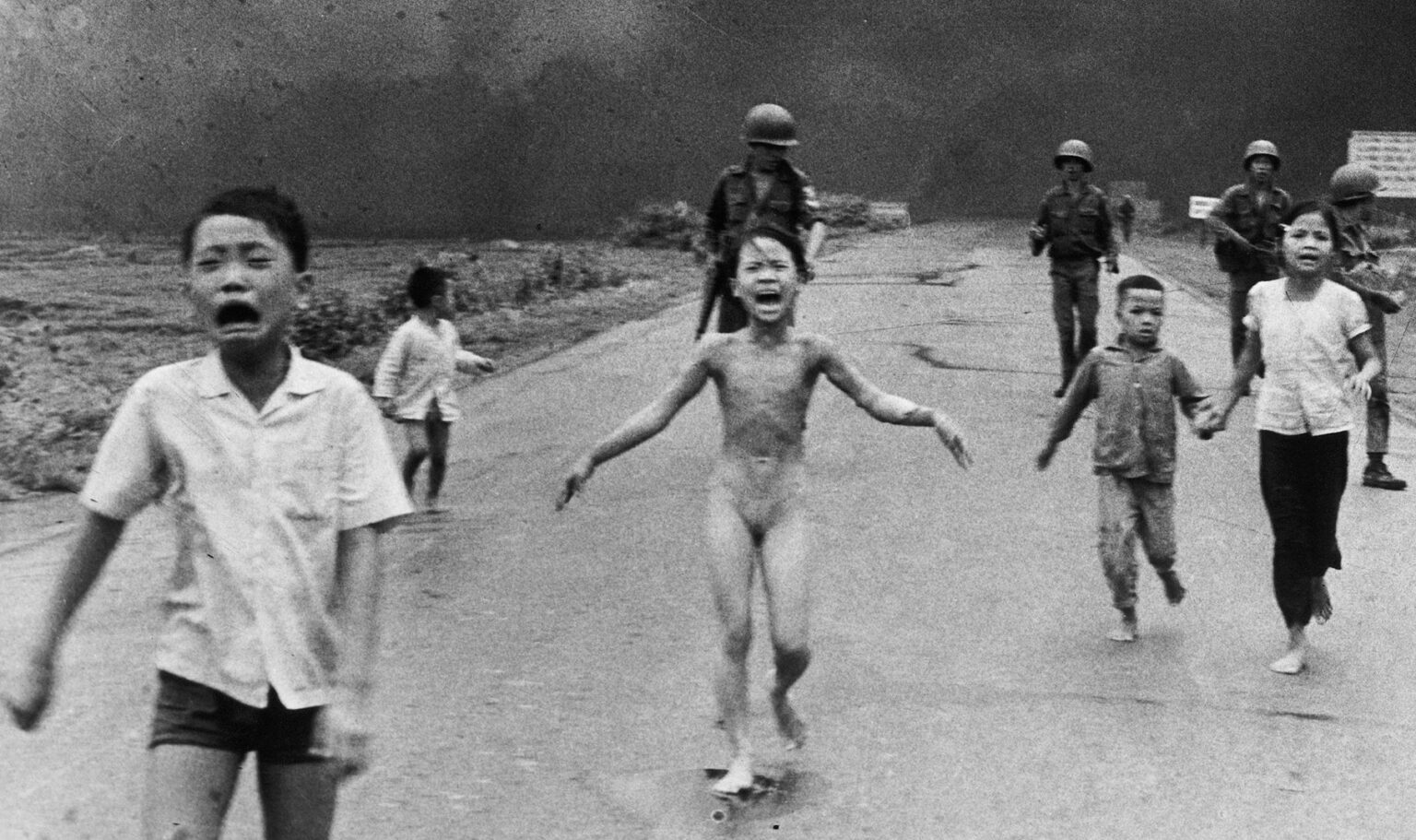 The ‘Terror of War’ Authorship Conversation Should Go Far Beyond One Photo A group of children, some crying and barefoot, run down a road toward the camera with smoke and armed soldiers in the background. The central child appears distressed and unclothed.