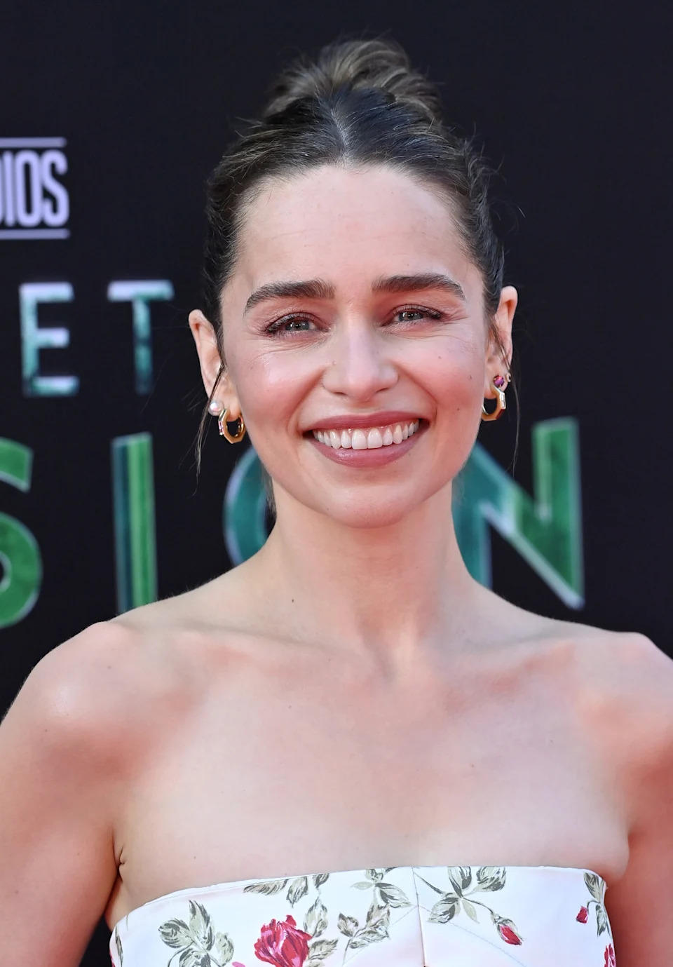 Person on the red carpet wearing a strapless floral dress, with hair styled in an elegant updo. Smiling for photos at a celebrity event