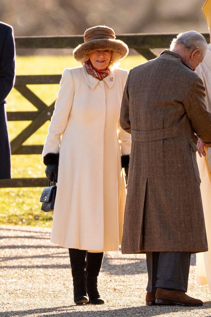 Queen Camilla smiling outside in white coatdress