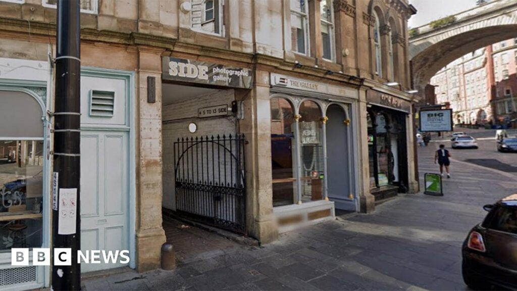 Newcastle’s former Side gallery site turned into Pilates studio Historic looking brick buildings with one of the fronts saying "Side photographic gallery" in large letters on a black storefront. There are doors and gates and windows of other shops on either side of the shopfront. There is a bridge in the background.