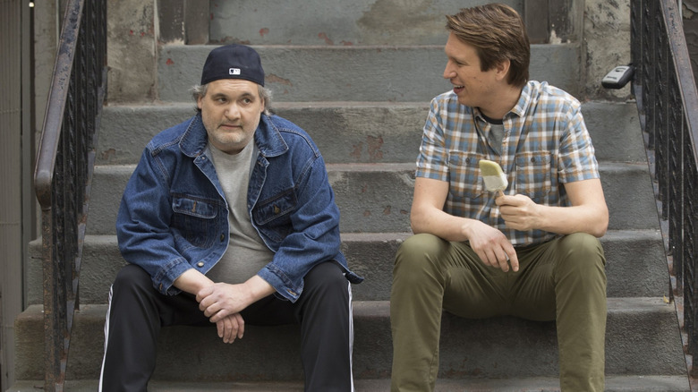 Artie Lange wears a backwards baseball cap while Pete Holmes eats an ice cream while sitting on a stoop in 