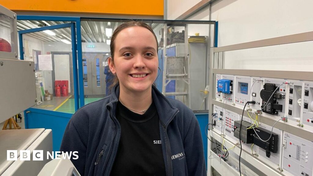 Scunthorpe apprentices prepare for wind turbine industry careers A young woman is wearing a Siemens branded blue fleece and is standing in a room surrounded by electrical equipment
