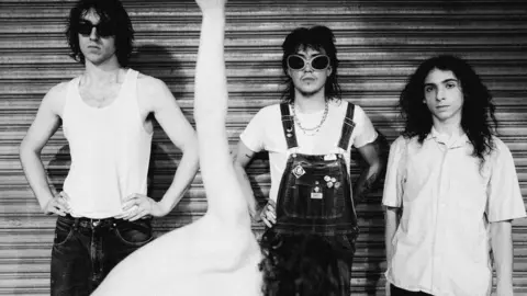 Lewis Evans Black and white promo shot of the band Geese, all stood near a metal shutter