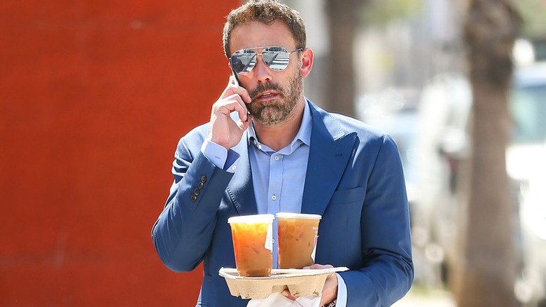 Ben Affleck talking on cellphone and holding a takeout tray with Dunkin' coffee