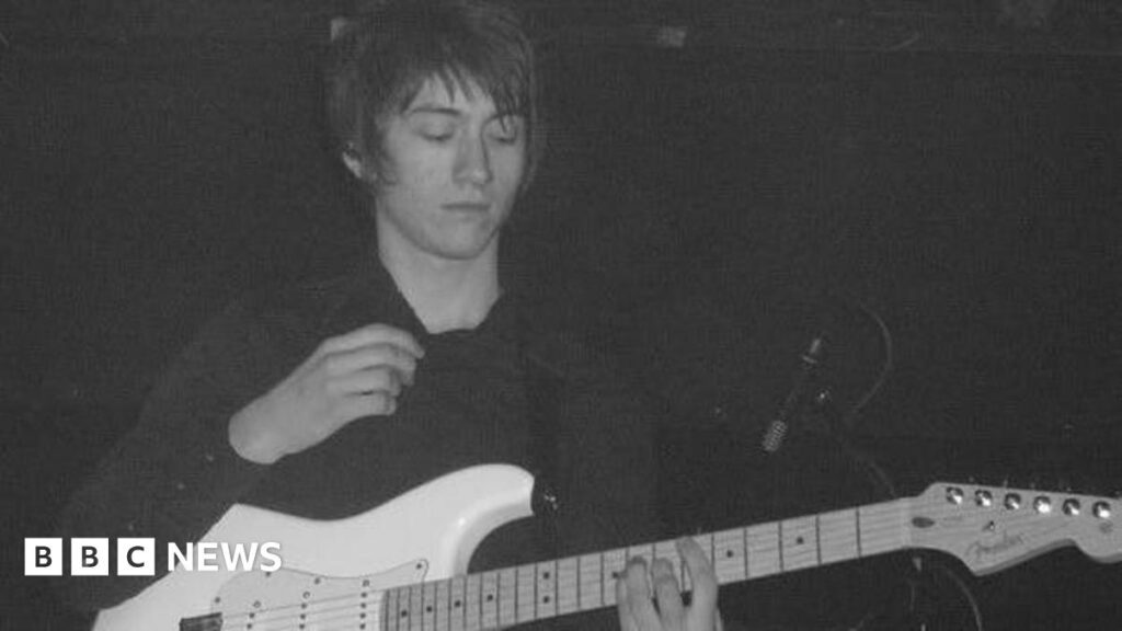 Arctic Monkeys producer’s pride at legendary debut 20 years on A young man with long dark hair playing a white guitar