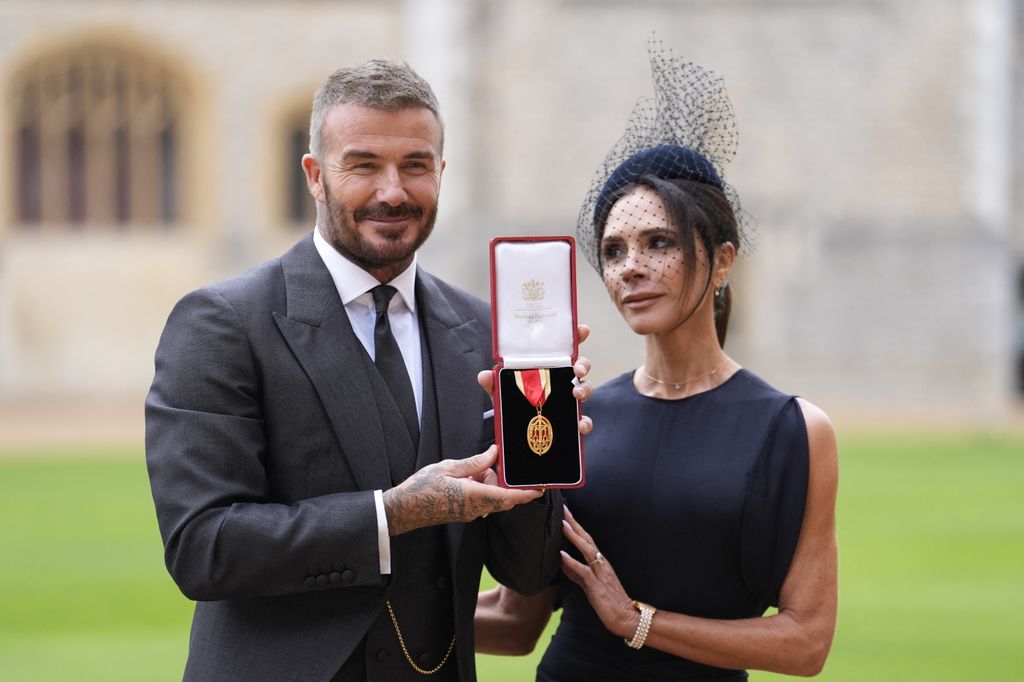 Former England footballer David Beckham (L) poses next to his wife singer and fashion designer Victoria Beckham (R) with his medal after being appointed as a Knight Bachelor (Knighthood) for services to sport and charity at an investiture ceremony at Windsor Castle on November 4, 2025. (Photo by Andrew Matthews / POOL / AFP) (Photo by ANDREW MATTHEWS/POOL/AFP via Getty Images)          