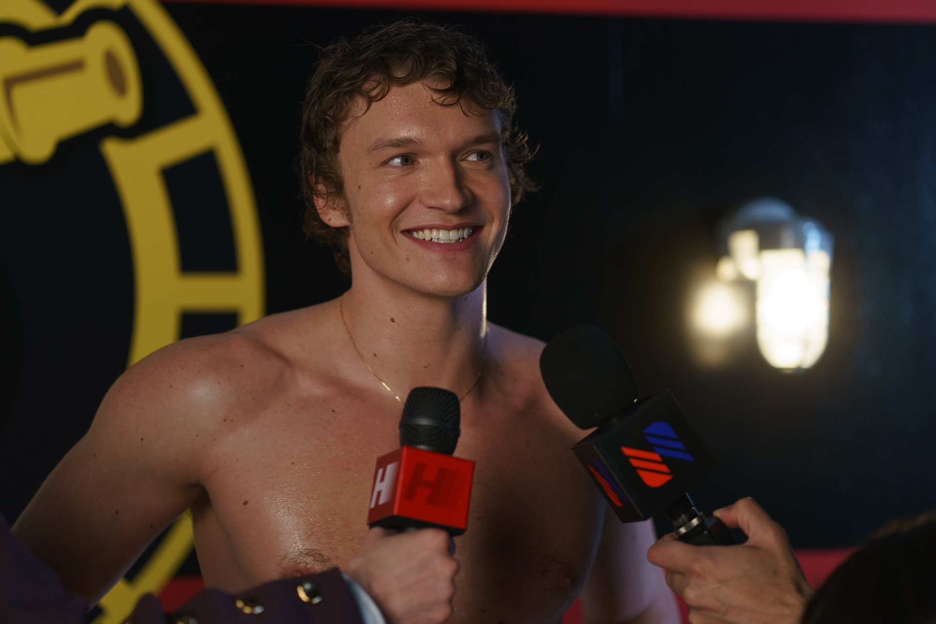Connor Storrie as Ilya Rozanov, shirtless and smiling while being interviewed.