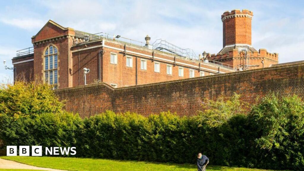 A general view picture of Reading Prison, a 19th Century jail with a man brushing a path outside its outer walls.