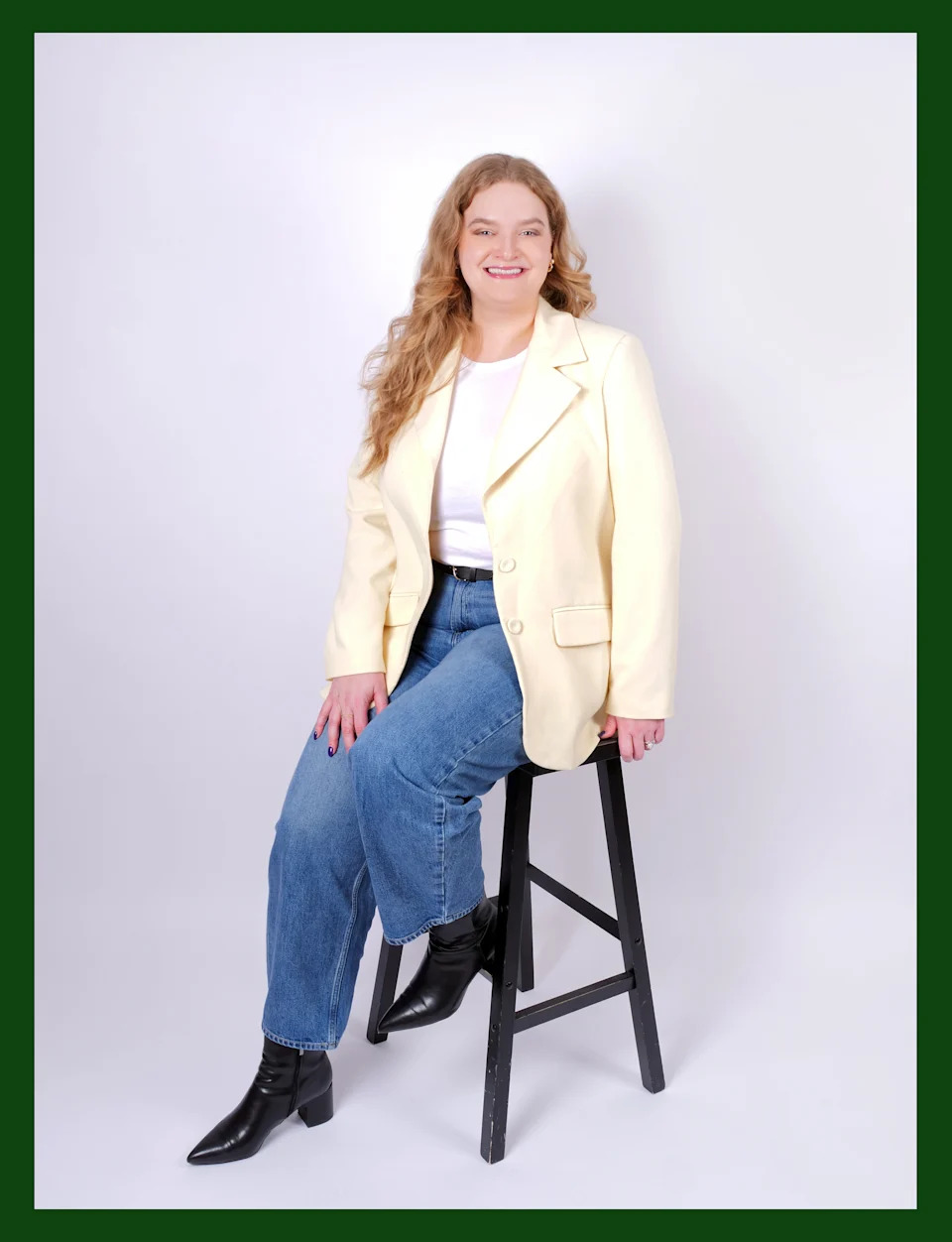 Kerry Justich sits on a wooden stool and poses for a full-length portrait