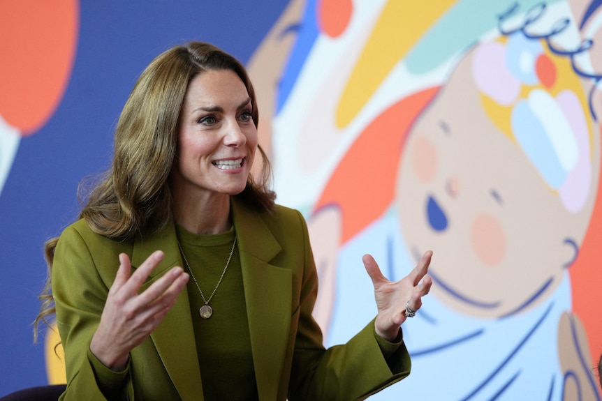 Kate Middleton speaking and gesturing with her hands, wearing a green suit.