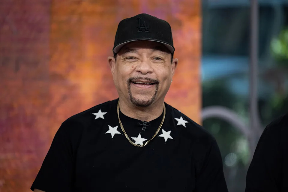 A man wearing a star-patterned shirt and a baseball cap smiles at the camera